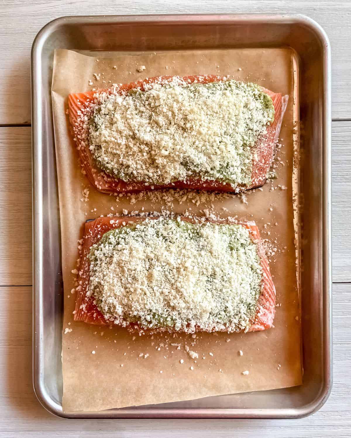 Fresh salmon filets on a parchment lined baking sheet topped with pesto and panko bread crumbs.