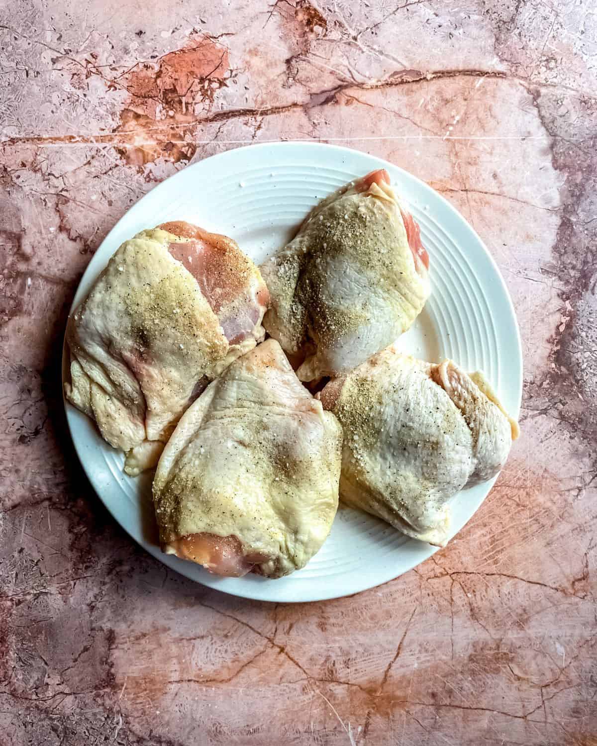 Raw chicken thighs, seasoned, on a white plate.