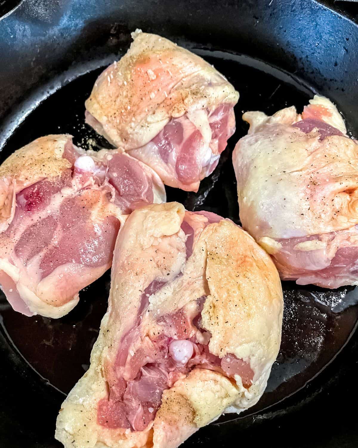 Raw chicken thighs, skin side down, searing in a cast iron skillet.