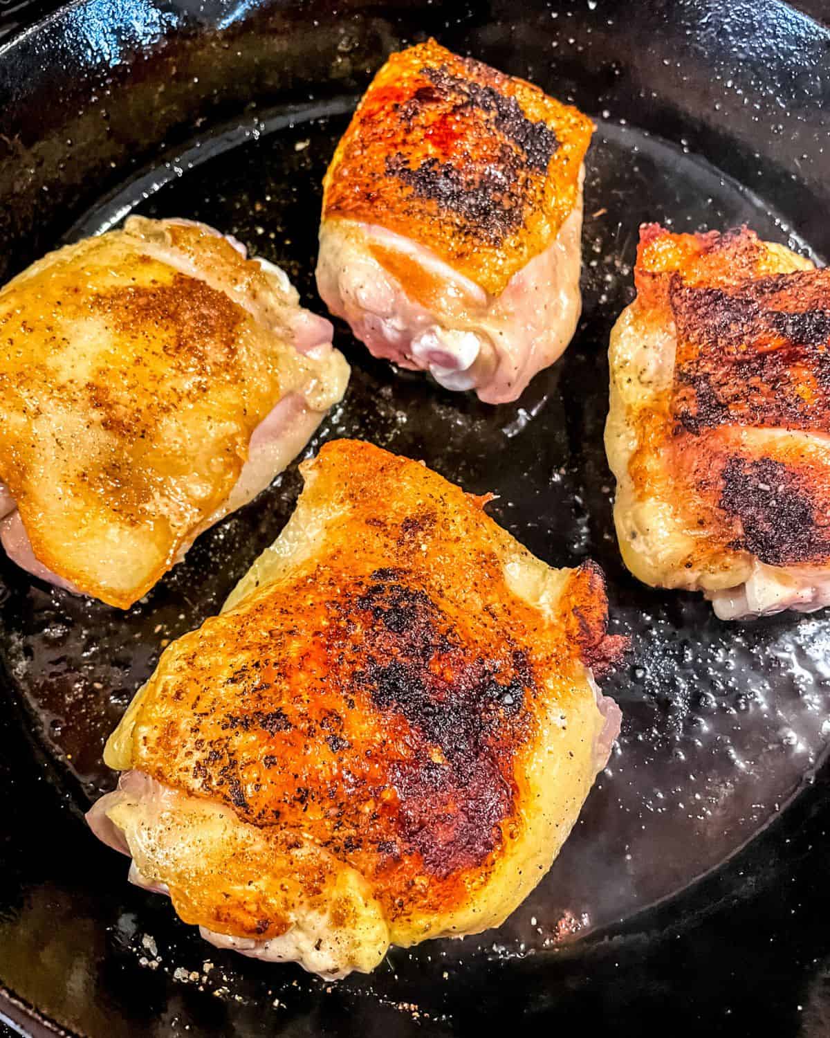 Seared chicken thighs in a skillet.