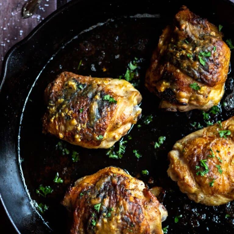 Cooked chicken thighs in a cast iron skillet, garnished with fresh parsley.