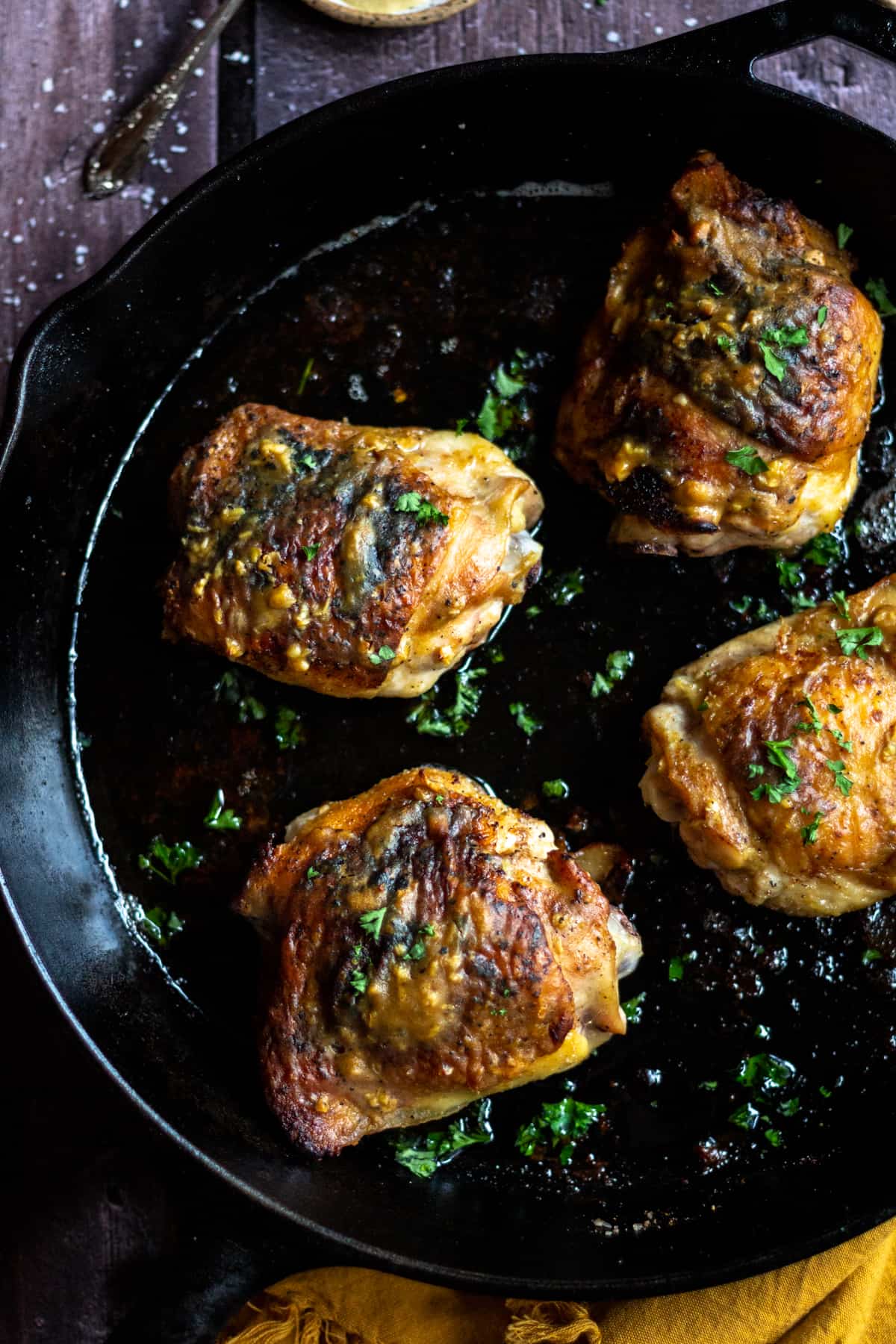 Dijon chicken thighs in a cast iron skillet, cooked, with a yellow napkin surrounding the pan.