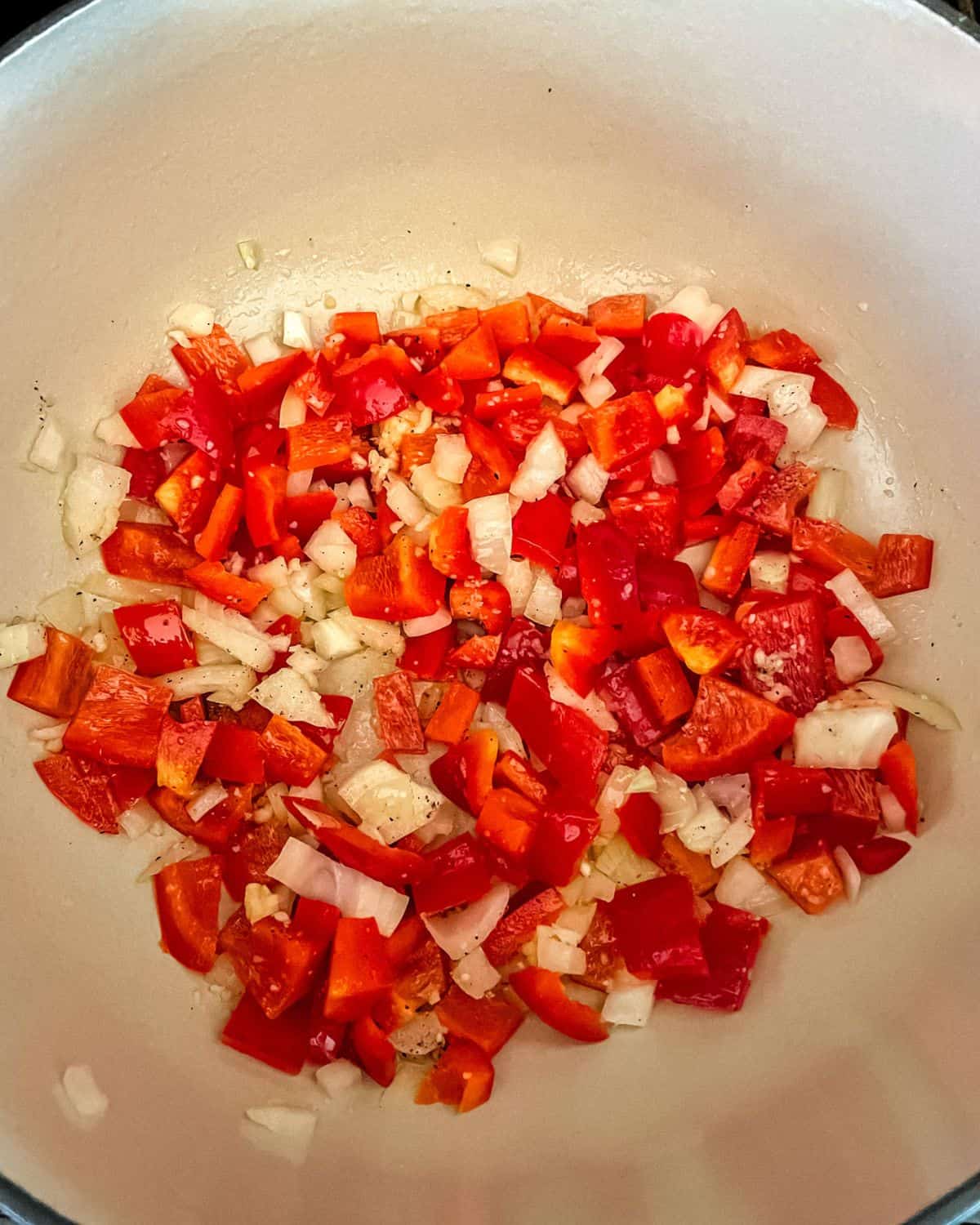Diced red peppers, onions, garlic, salt and pepper sauteing in the bottom of a cast iron Dutch oven.