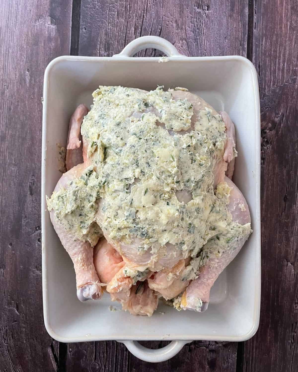 Garlic and herb butter slathered on a raw chicken.