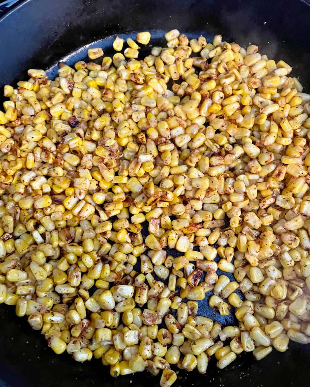 Cooked corn in a skillet with blackening seasoning mixed in.