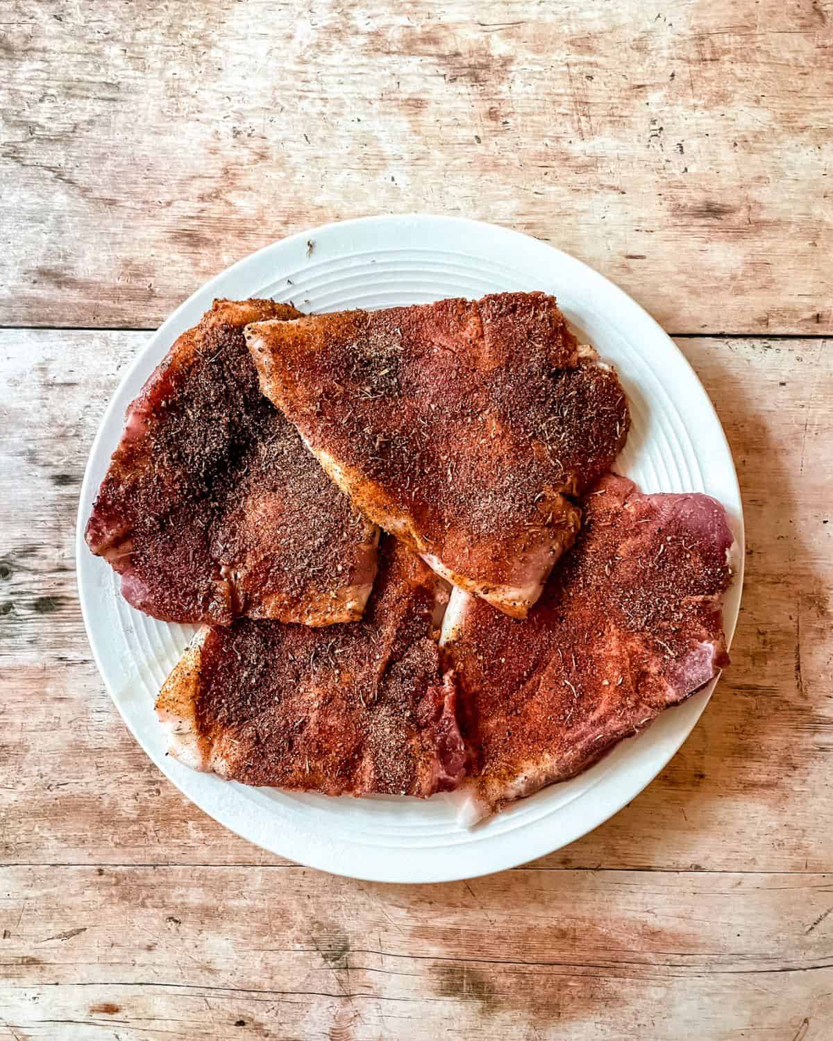 Raw pork chops, seasoned with blackening blend, on a white plate.
