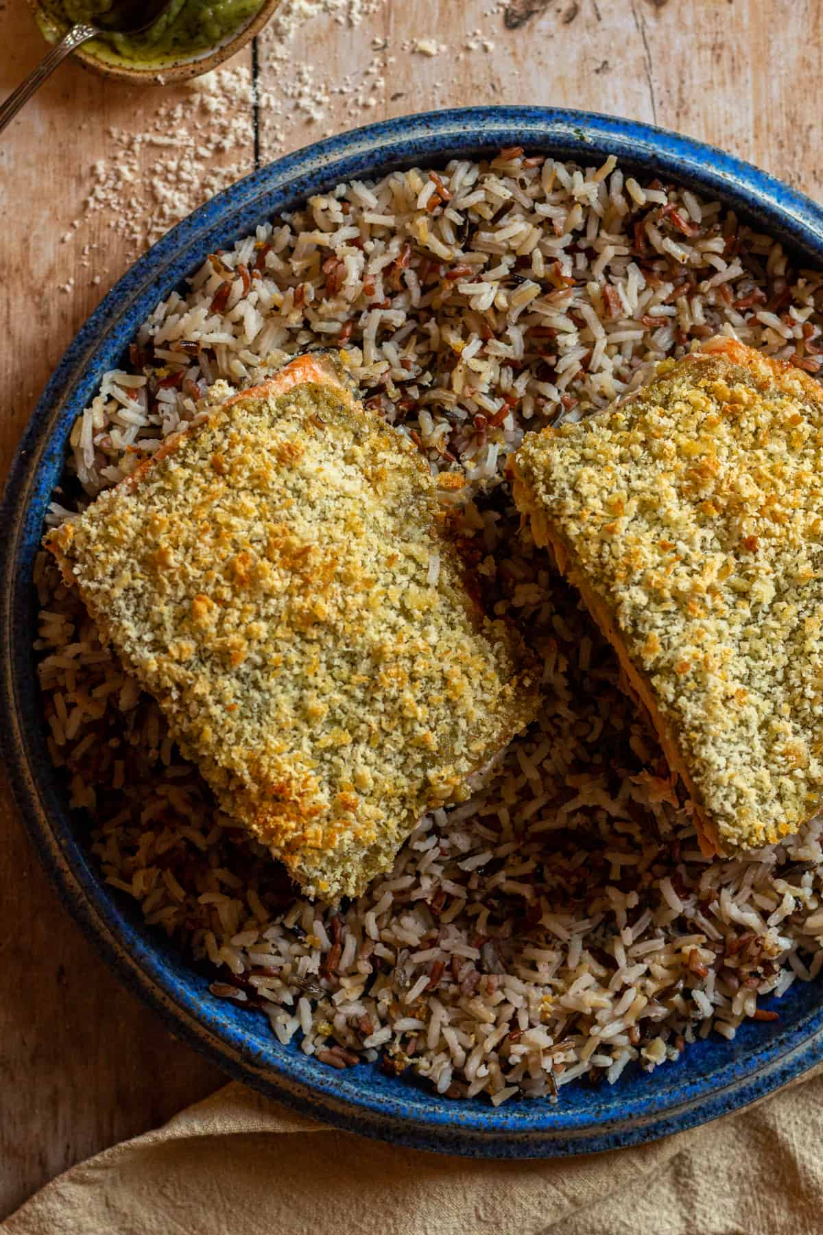 Pesto crusted salmon with panko bread crumbs and parmesan cheese, on a blue plate, over a bed of wild rice.