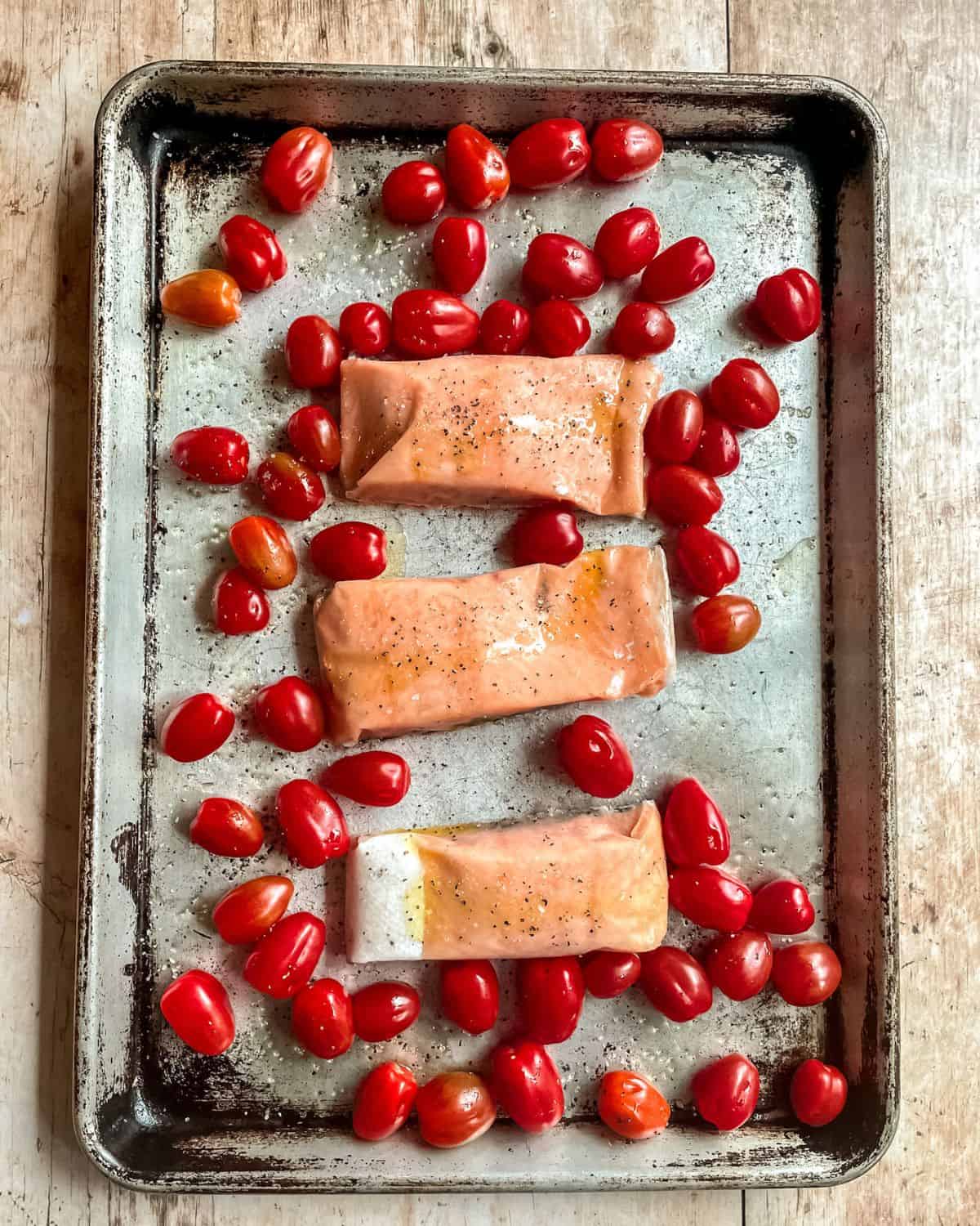 Frozen salmon and cherry tomatoes on a baking sheet, ready to go in the oven.