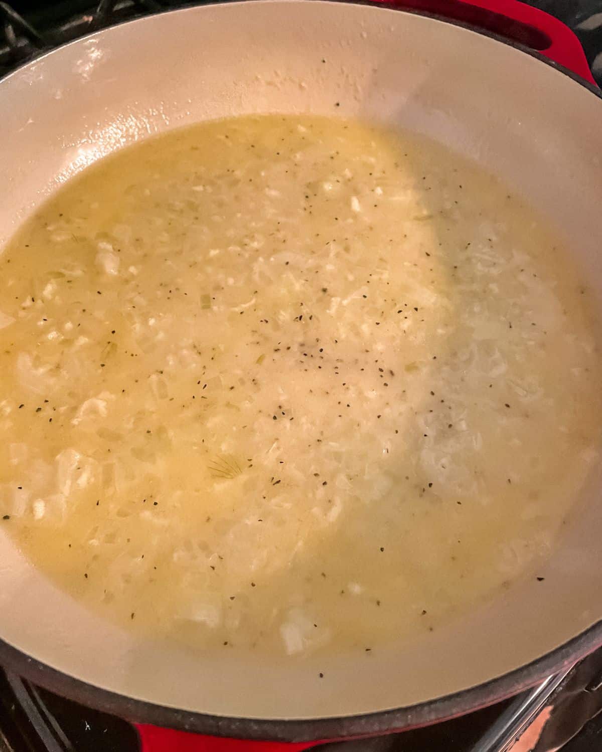 Garlic, butter, lemon and white wine sauce in a large skillet with red handles.