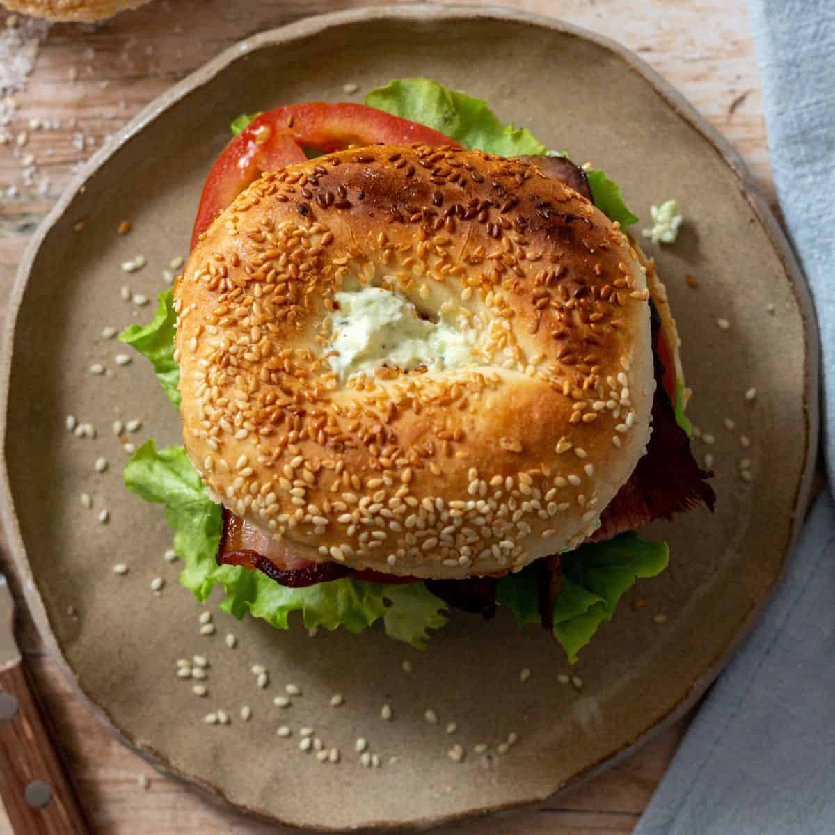 Bagel BLT on a round plate with a blue napkin.