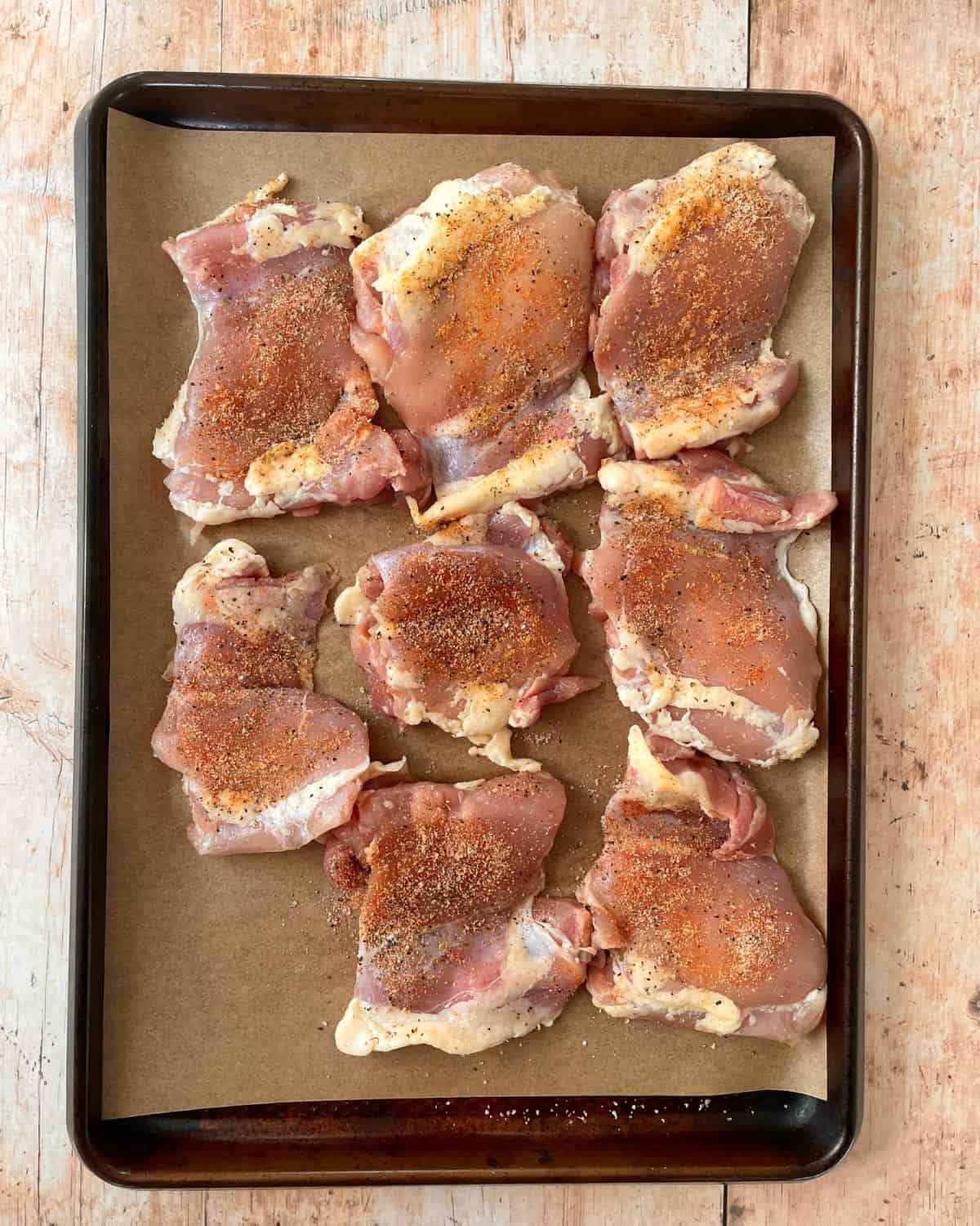 Chicken thighs on a parchment lined sheet pan with dry seasonings.