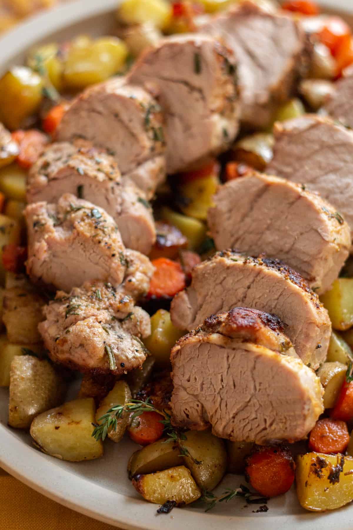 Cast Iron Skillet Pork Tenderloin on a round plate with roasted potatoes and carrots. Garnished with fresh thyme.