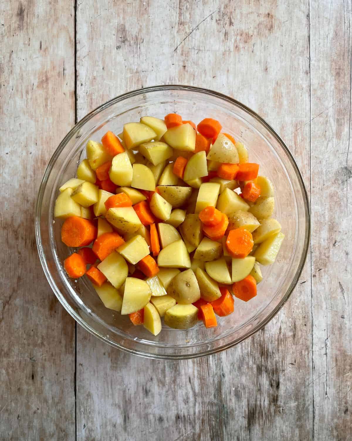 Chopped potatoes and carrots in a glass bowl.