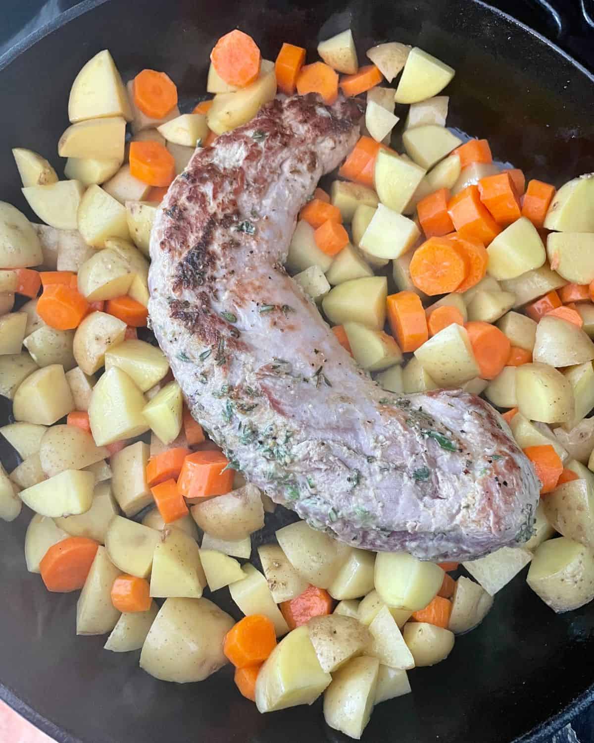 Chopped baby potatoes and carrots added to the cast iron skillet with the pork tenderloin.