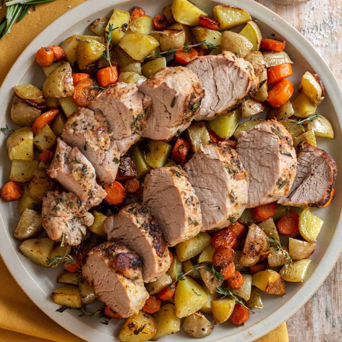 Cast Iron Skillet Pork Tenderloin on a round plate with roasted potatoes and carrots. Garnished with fresh thyme.