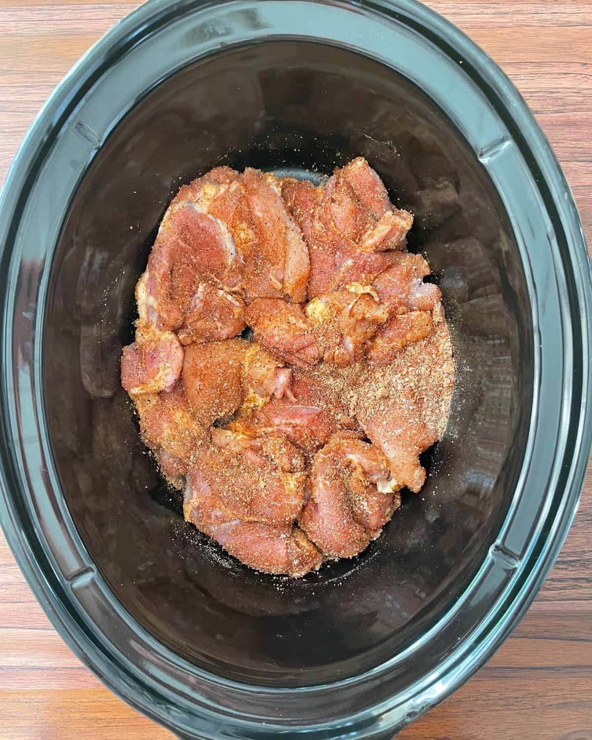Boneless chicken thighs seasoned with BBQ seasoning in a slow cooker.