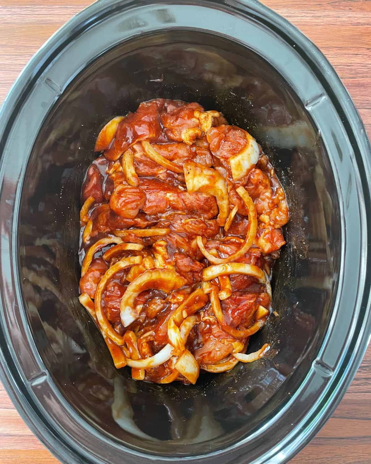 BBQ sauce is tossed into the onions and chicken thighs in the slow cooker.
