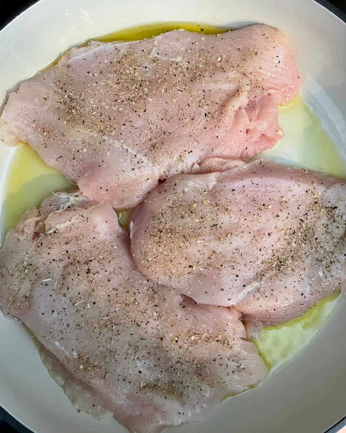 Seasoned chicken breasts cooking in olive oil in a skillet.