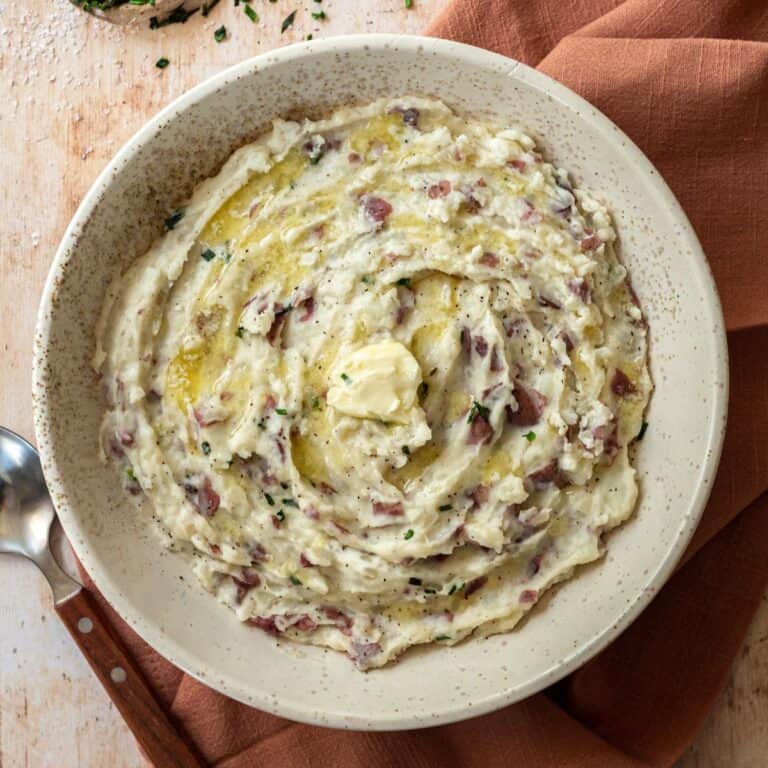 Redskin mashed potatoes with cream cheese in a beige bowl, on a pink napkin, with a spoon.