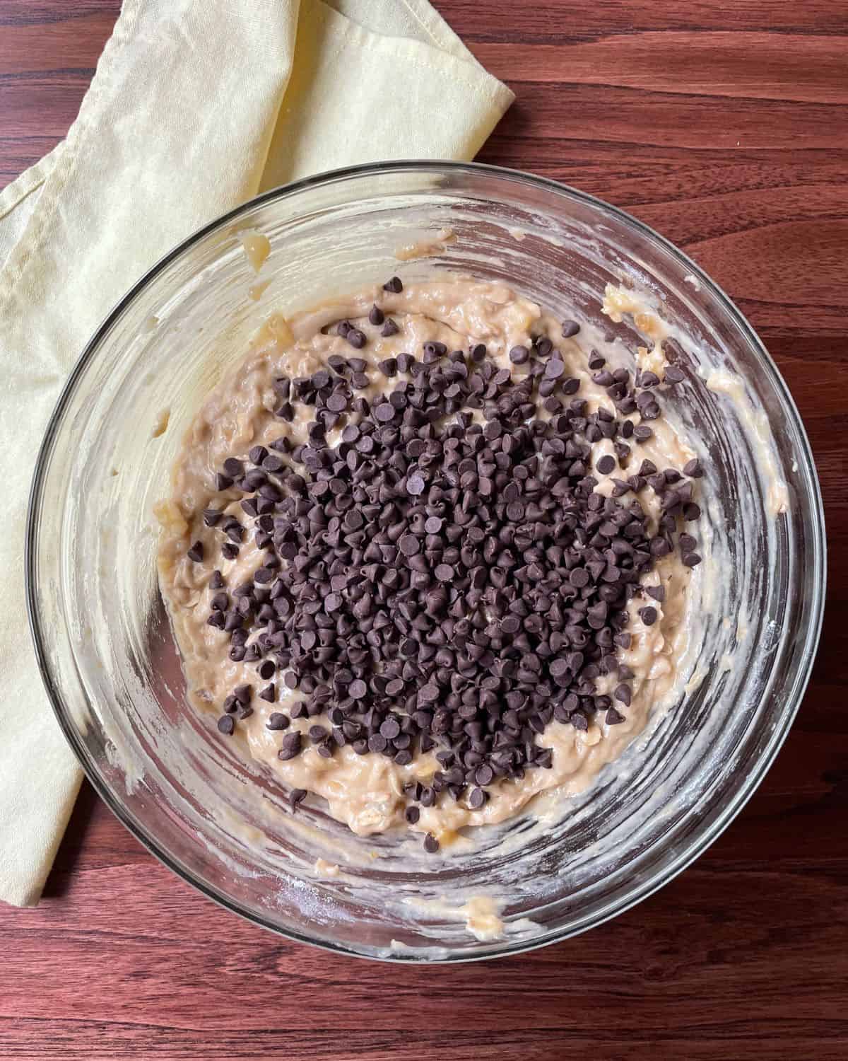 Mini chocolate chips are added to the mixed ingredients in a glass bowl.