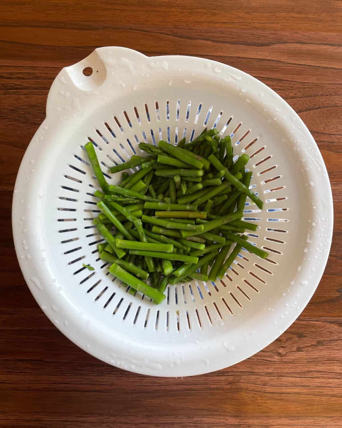 Cooked asparagus pieces in a white plastic strainer.