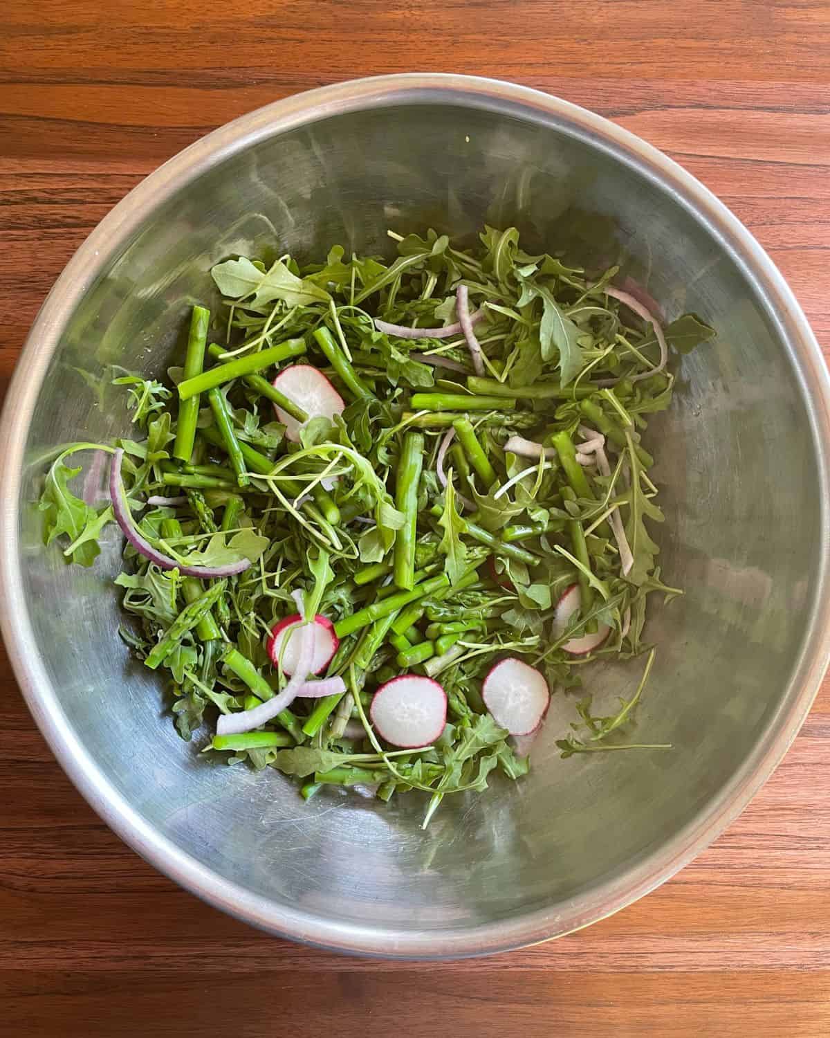 Arugula, sliced radishes, cooked asparagus, and sliced red onion in a large mixing bowl.