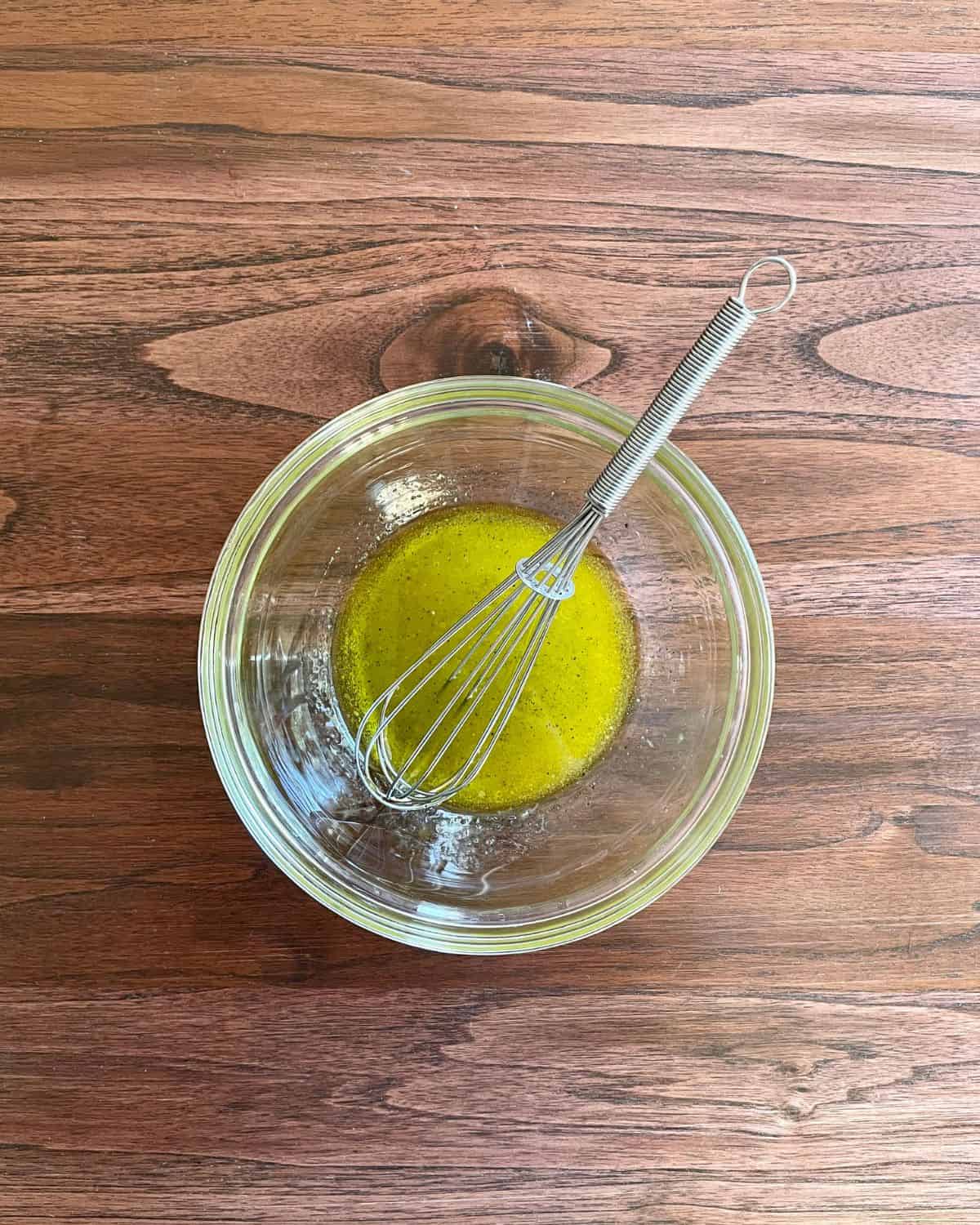Olive oil, lemon juice, salt, and pepper in a small glass bowl with a whisk.