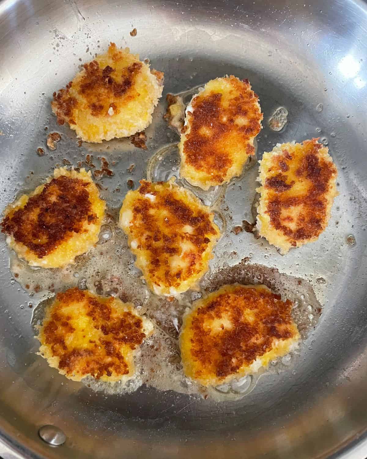 Panko goat cheese frying in olive oil in a stainless steel frying pan.