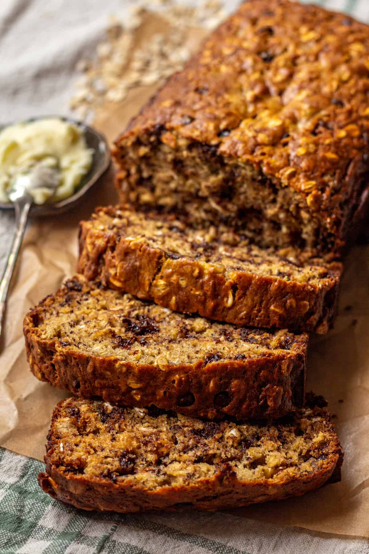 Sliced Oatmeal Banana Bread on parchment paper with a small dish or butter with a spoon.