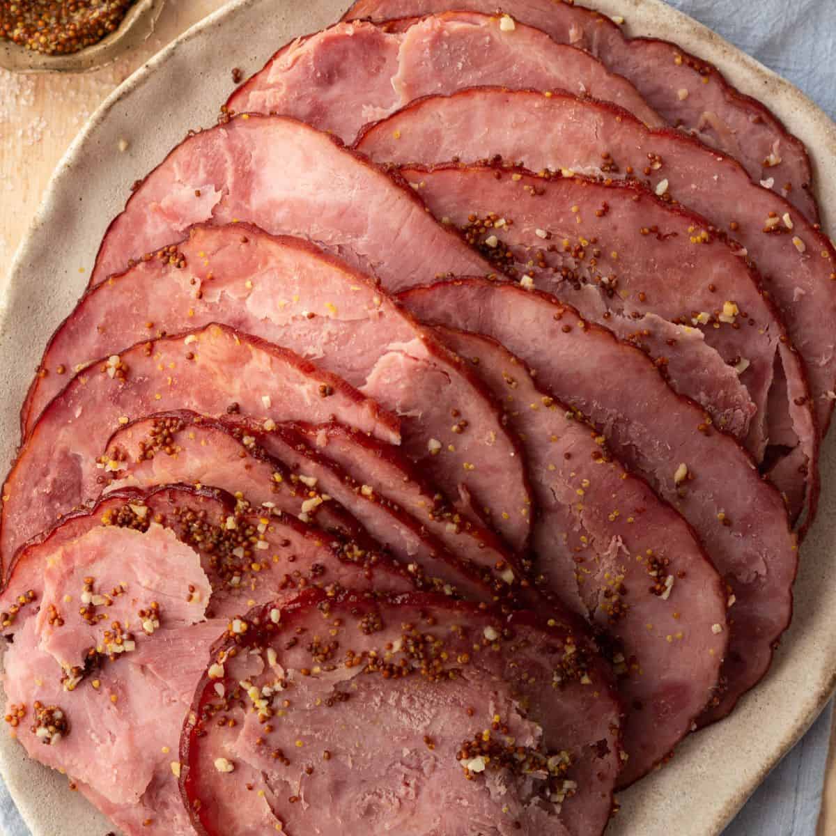 Sliced spiral ham with maple dijon glaze, on a round plate and a light blue napkin.