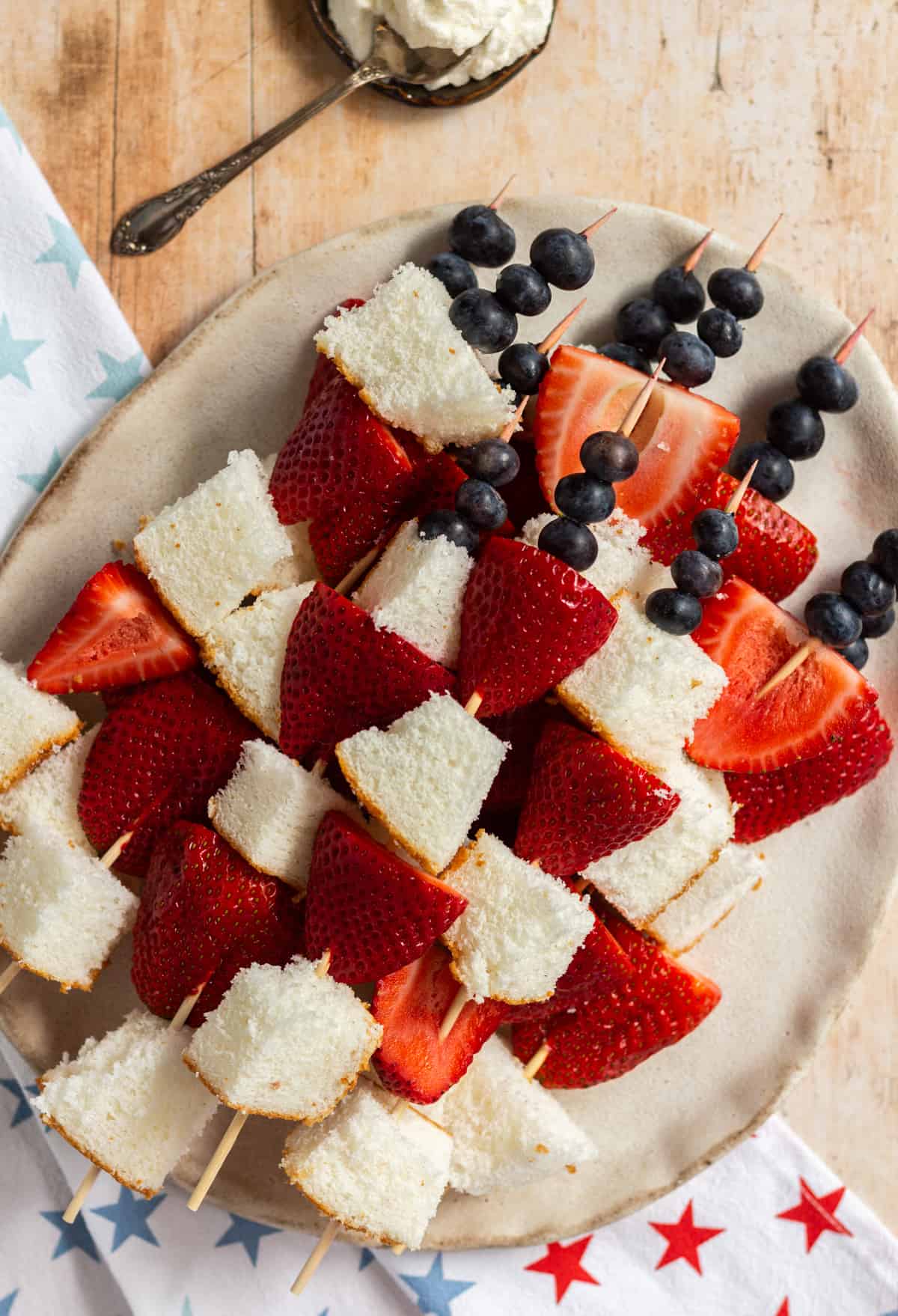 Sliced strawberries, angel food cake, and blueberries on a skewers. They're on a plate sitting on top of a red, white, and blue starred napkin.