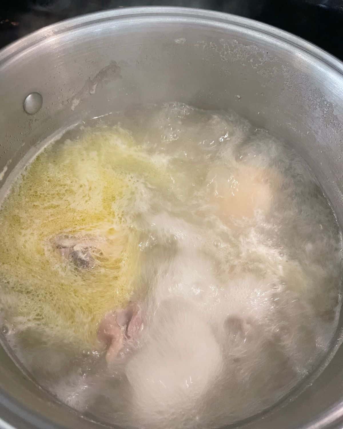 Chicken thighs in a stock pot in boiling water with chicken bouillon added.