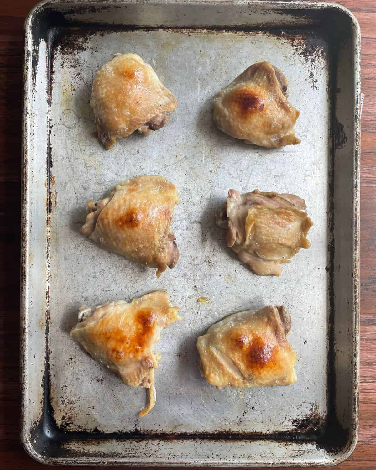 Boiled chicken thighs on a sheet pan that have been broiled until the skin turns golden brown.
