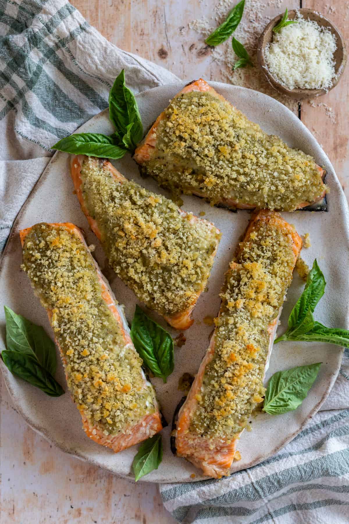 Four filets of Pesto Crusted Salmon with panko on a large round platter, garnished with fresh basil.