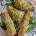 Panko crusted salmon recipe with pesto, on a round plate, garnished with fresh basil.