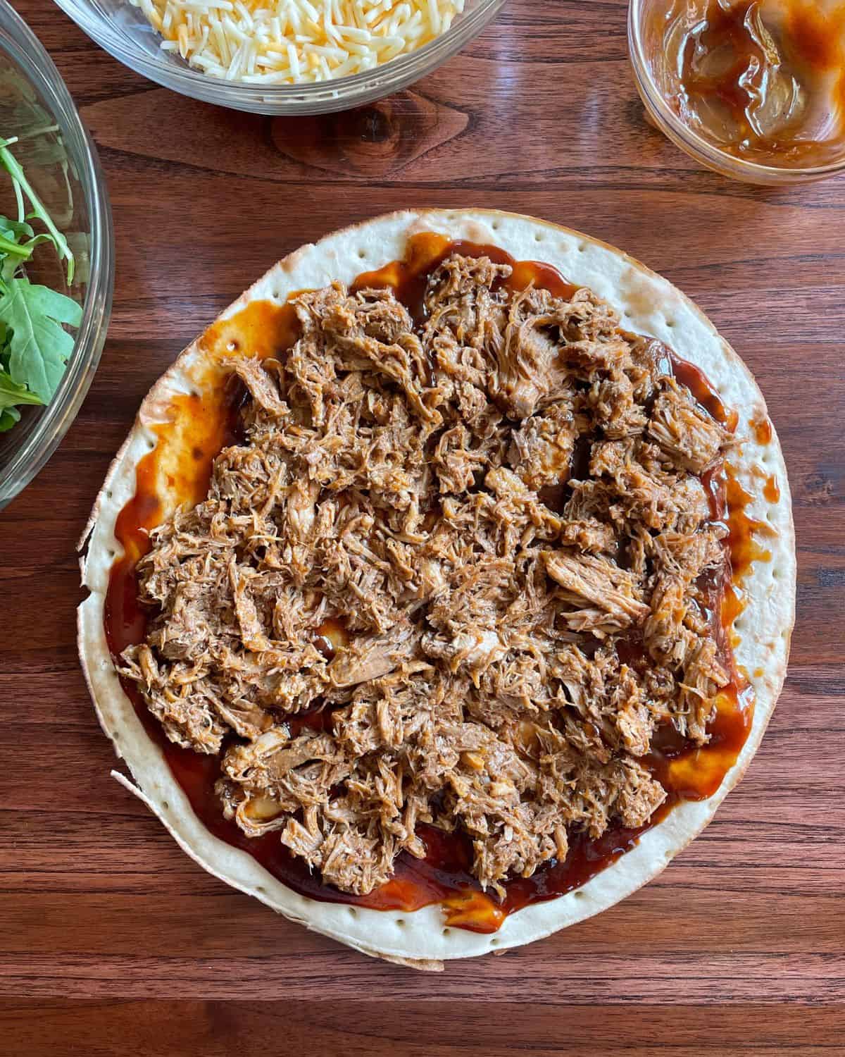 Pizza shell covered in BBQ sauce and pulled pork.