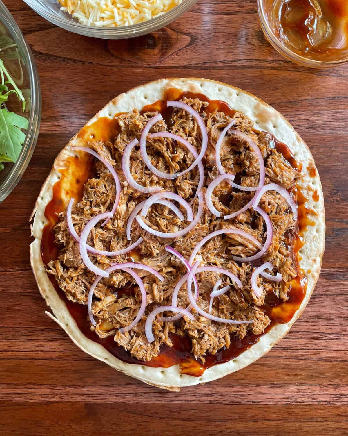 Pizza shell topped with sauce, pork, and sliced red onions.