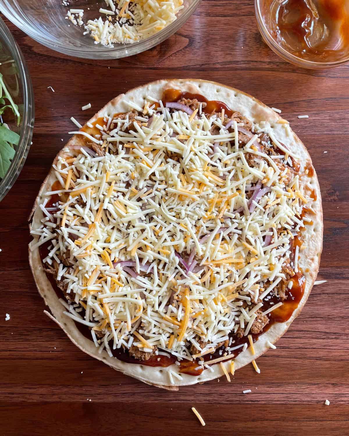 Pizza shell topped with sauce, pork, sliced red onions, and cheddar cheese.