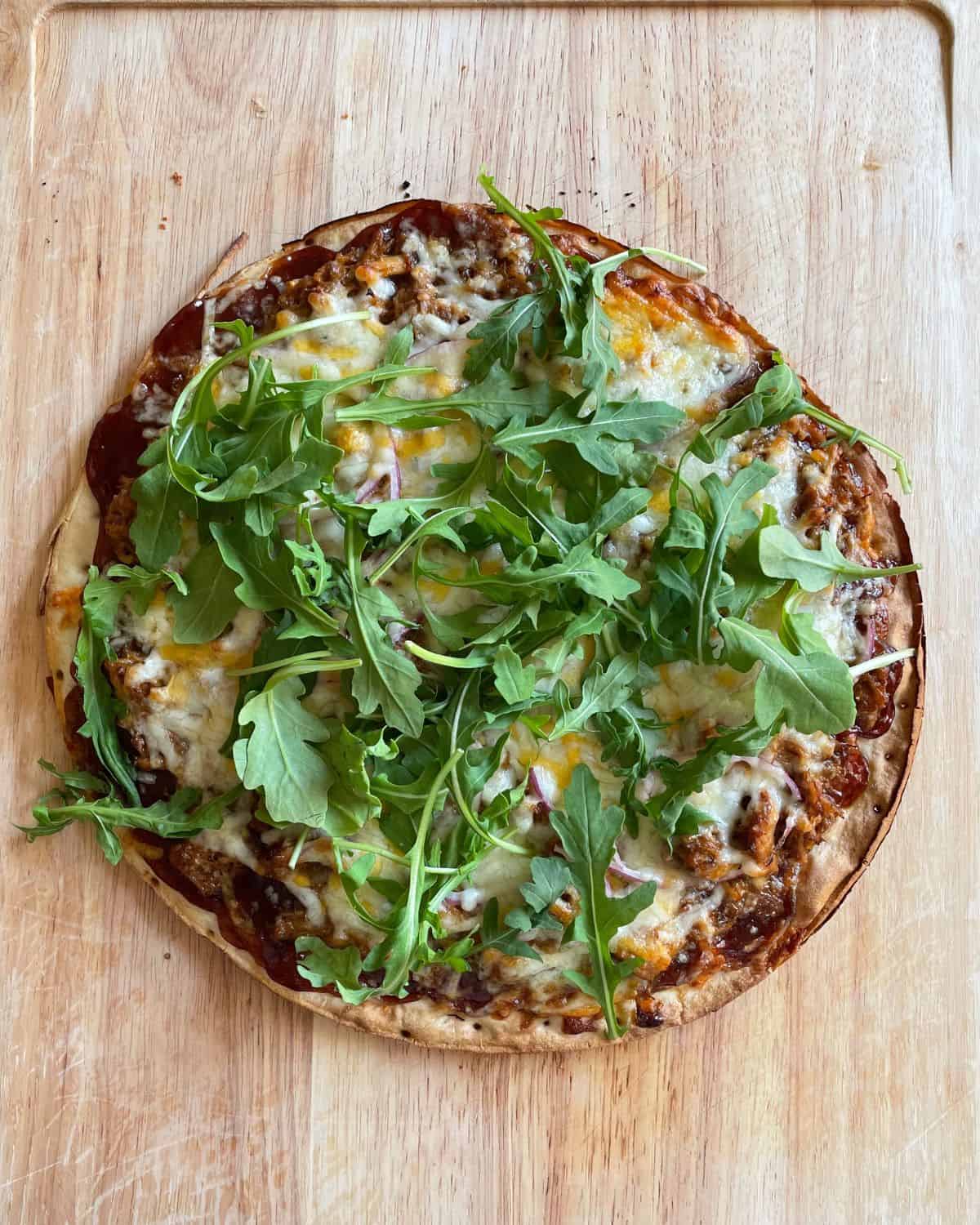 Cooked shredded pork pizza topped with fresh arugula.