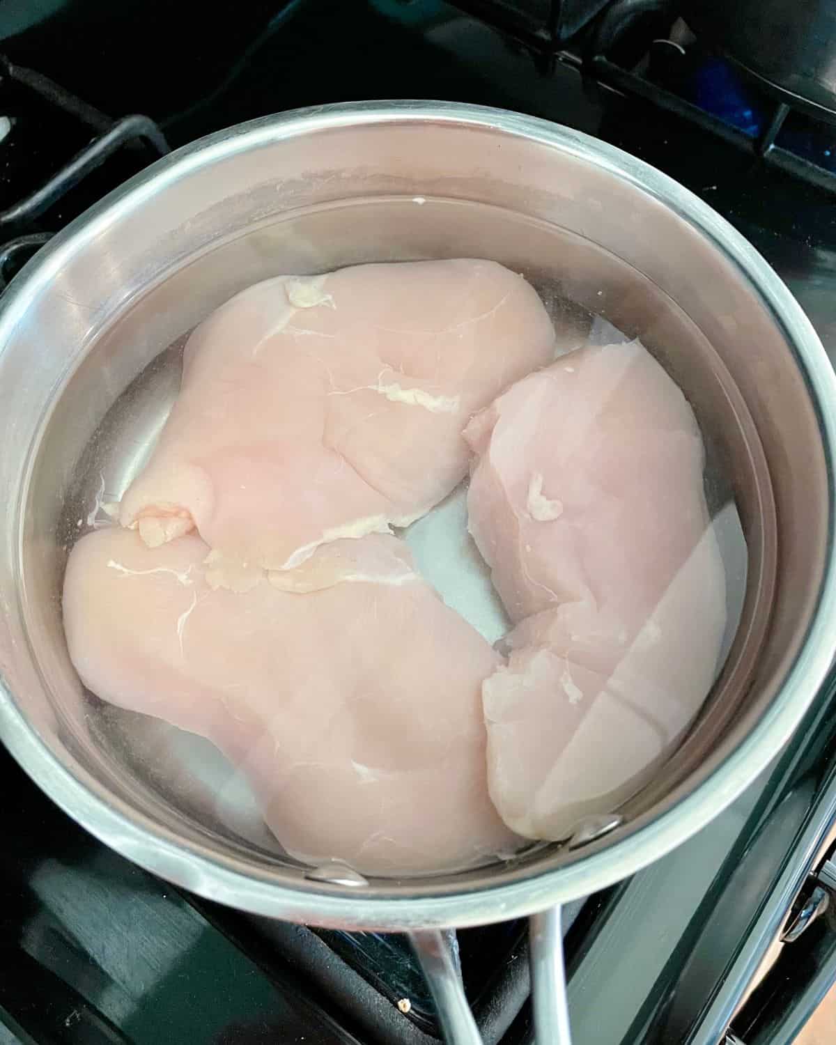 Raw chicken in water in a saucepan.