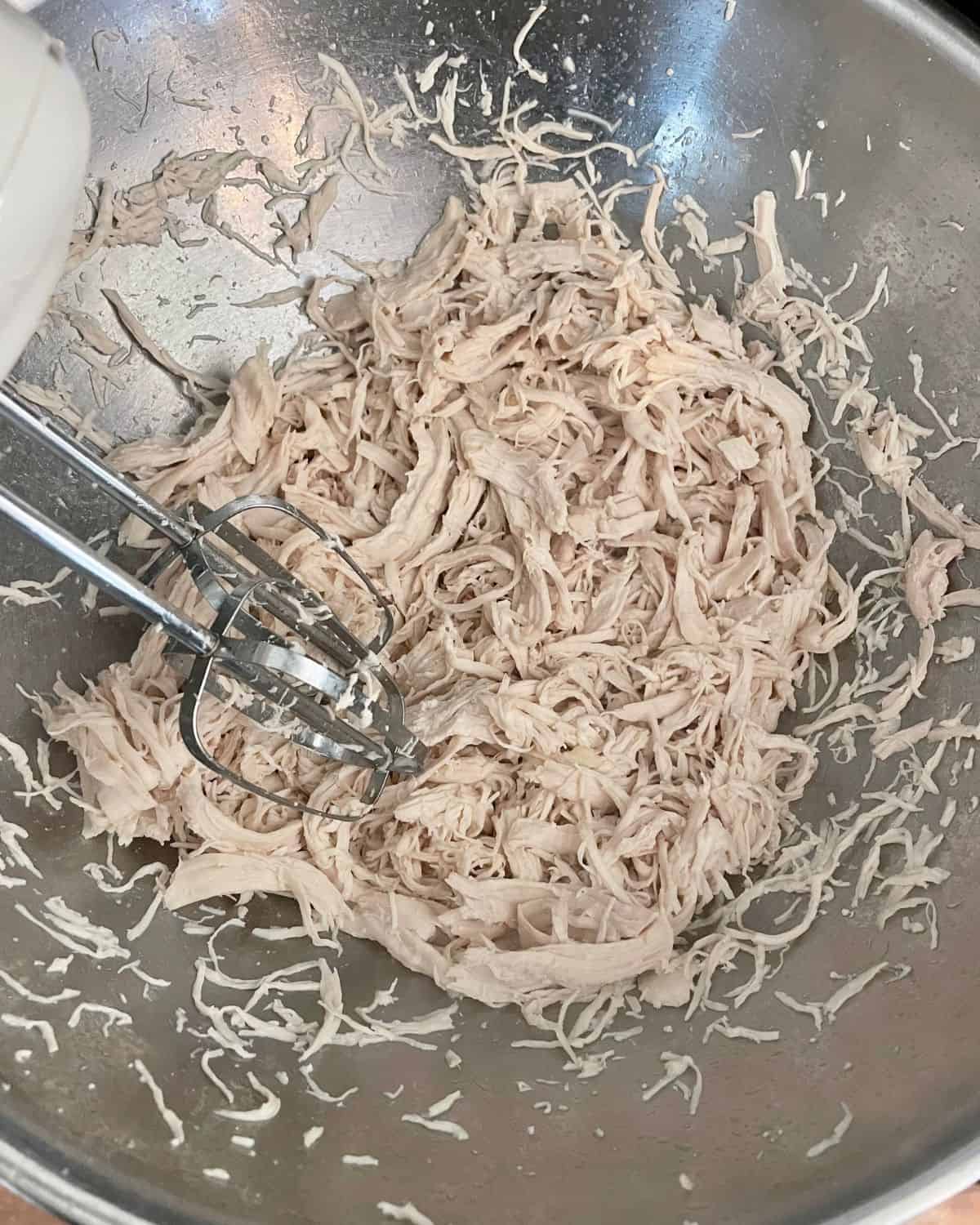 Shredded chicken breast in a large bowl with an electric mixer.