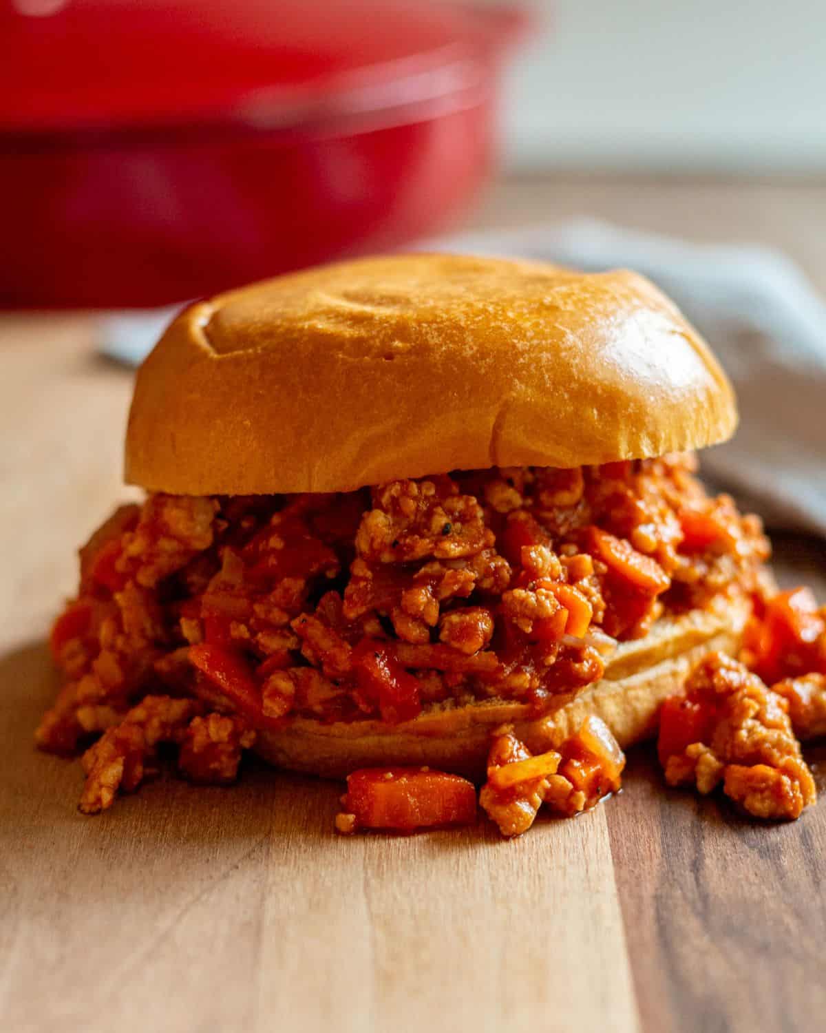 Sloppy joes on a bun with a red pan in the background.