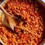 Ground chicken sloppy joes in a skillet with a wooden spoon scooping up some of the mixture.