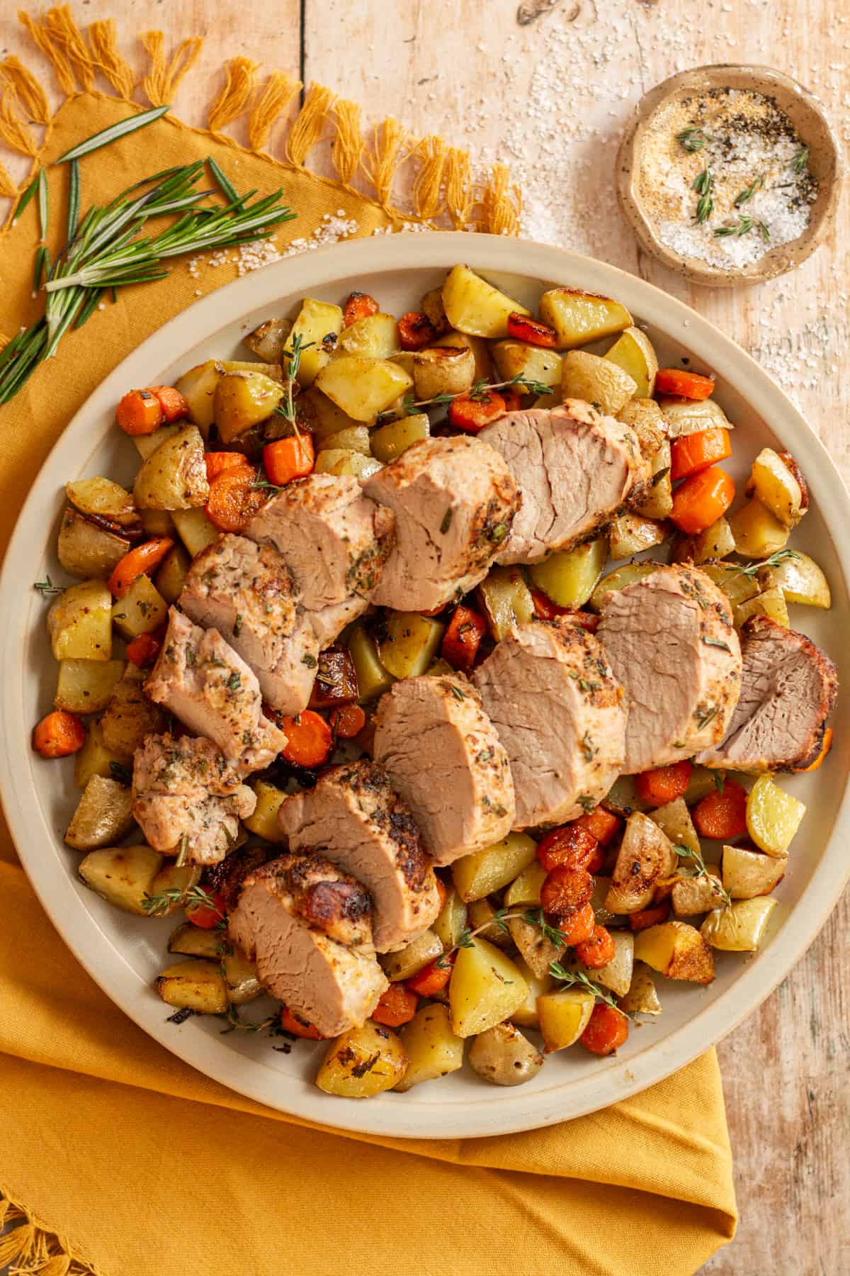 Sliced cast iron pork tenderloin on a bed of roasted carrots and potatoes, garnished with fresh thyme and rosemary.