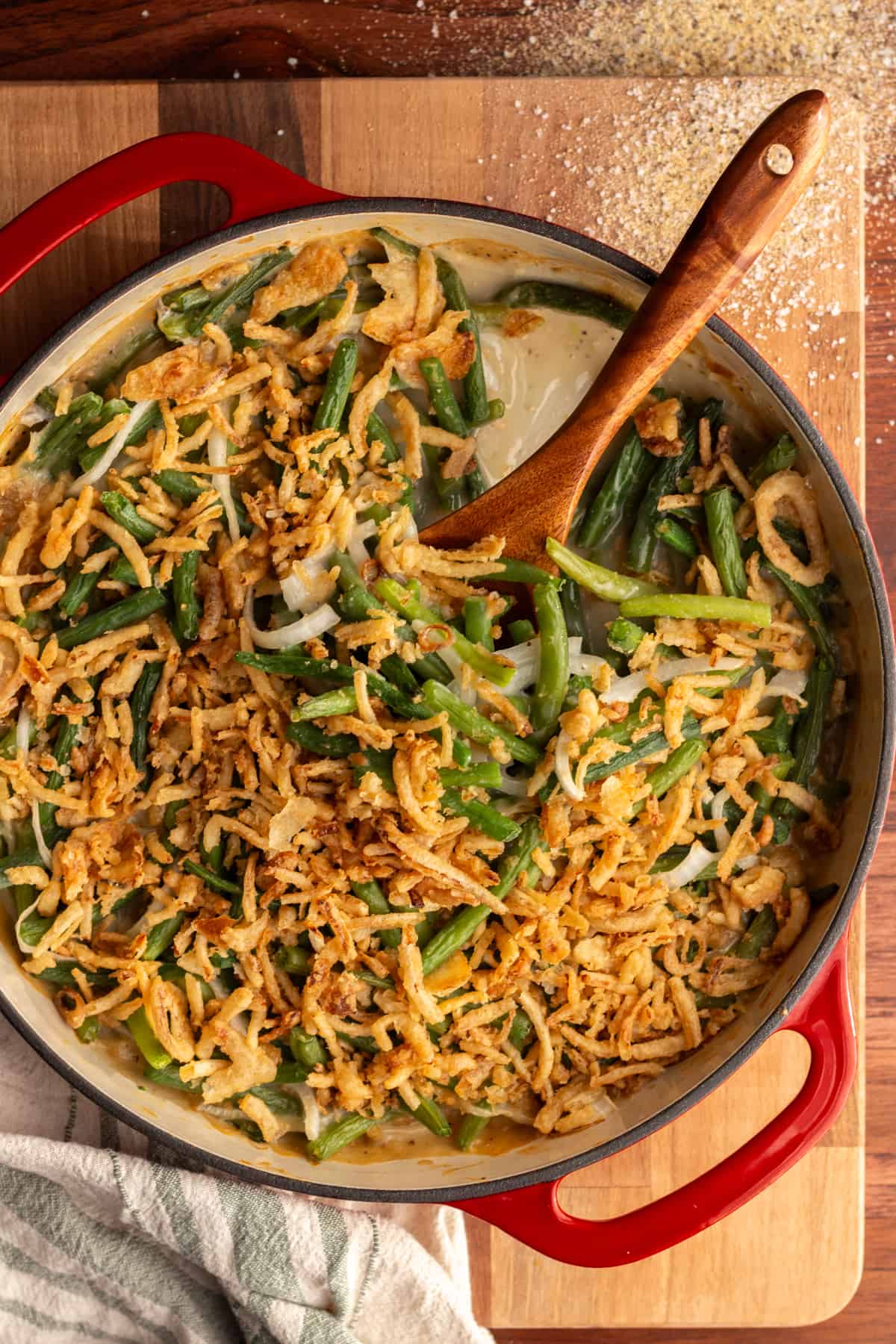 Easy green bean casserole with cream of chicken soup in a round, red casserole dish with a wooden spoon.