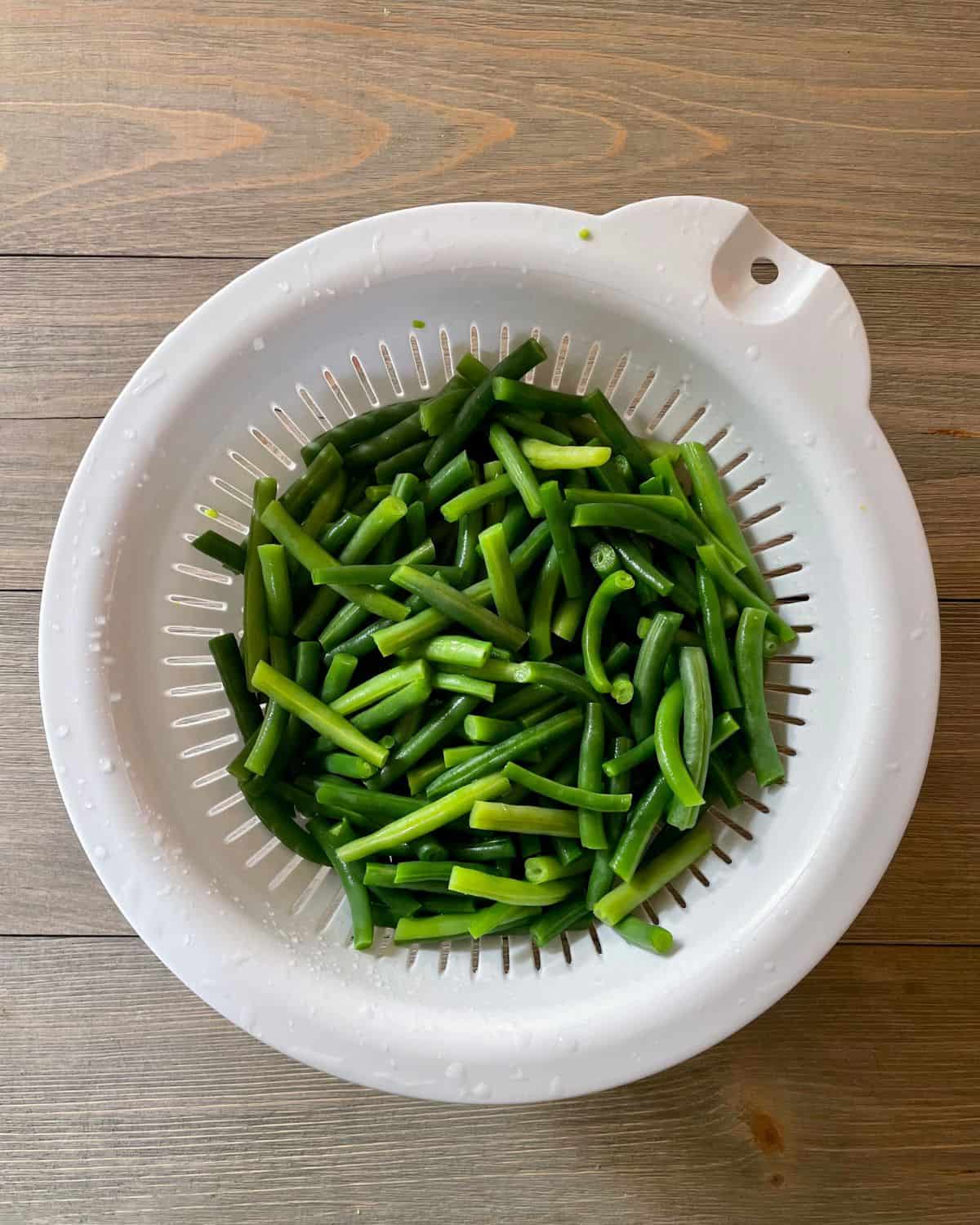 Blanched green beans in a strainer.