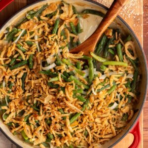 Green bean casserole with cream of chicken soup in a round, red casserole dish with a wooden spoon.