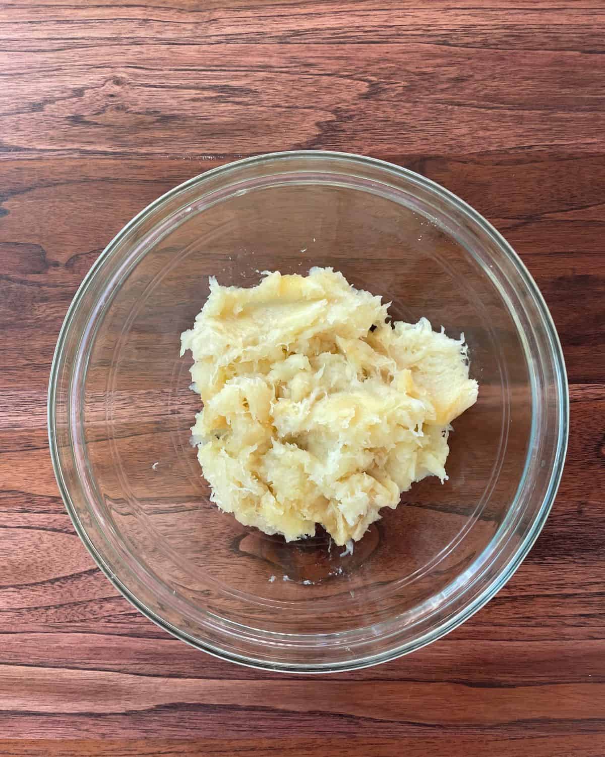 Cooked mashed potato squash scooped out of the flesh, in a glass mixing bowl.