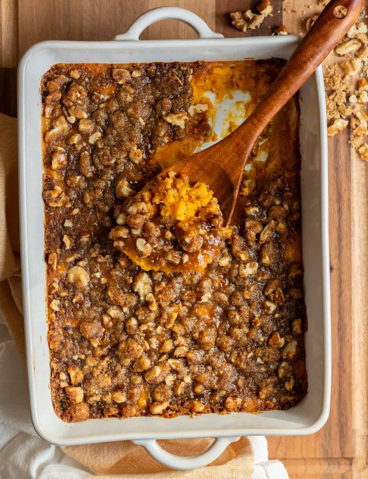 Cooked sweet potato casserole with walnuts in a casserole dish, with a wooden spoon scooping some up.