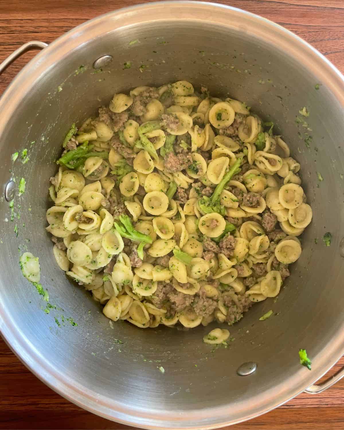 Sausage, broccoli, and pasta mixed together in a stainless steel pot.